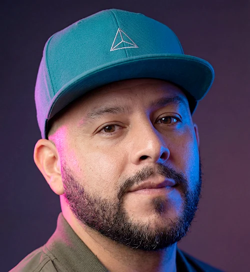 David Anchondo, portrait in a teal cap under pink and blue studio light